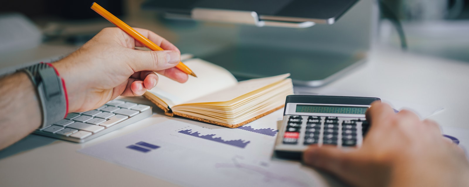An accountant working through client figures with a calculator, notebook and printed charts